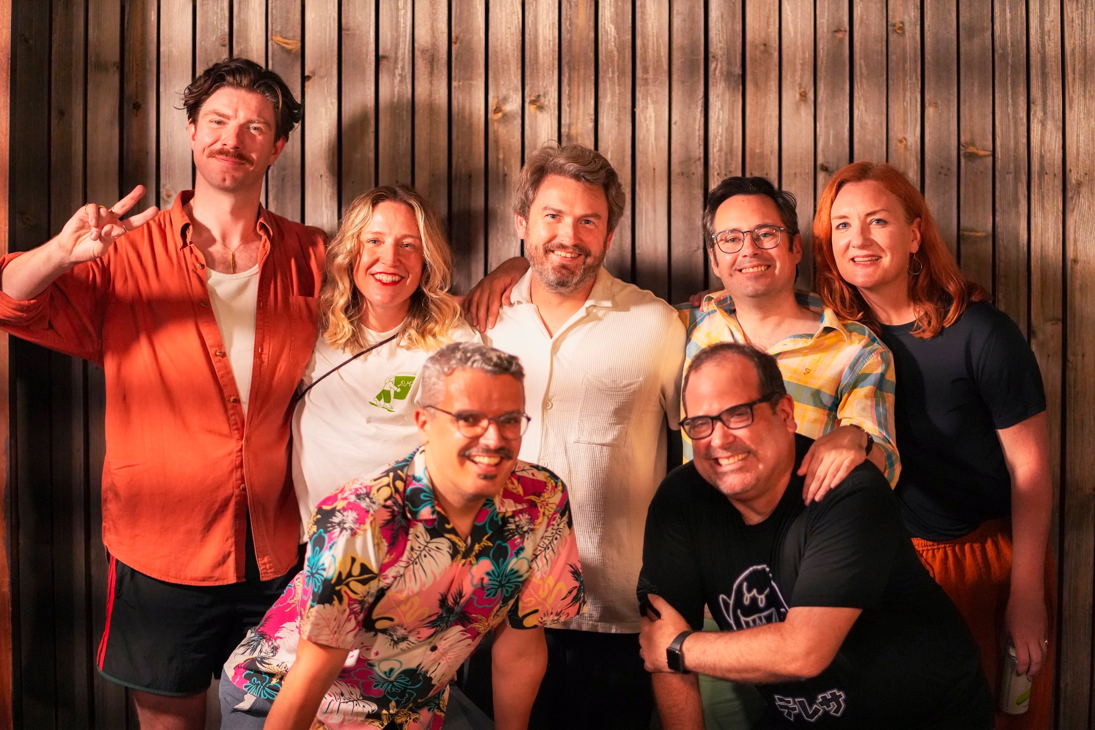 The improv group auto-correbt posing for a group photo in front of a wood panel wall