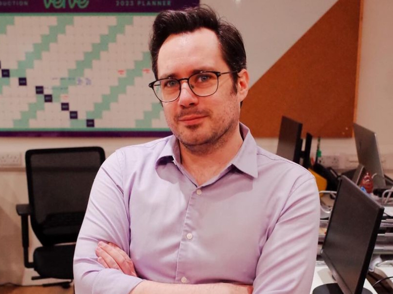 A photo of a handsome man standing with crossed arms weraing a purple shirt