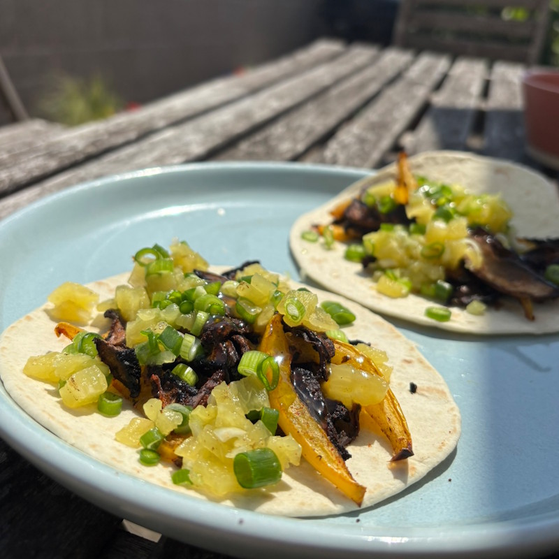 Mushrooms tacos on a blue plate on a wooden table outside in the sun.